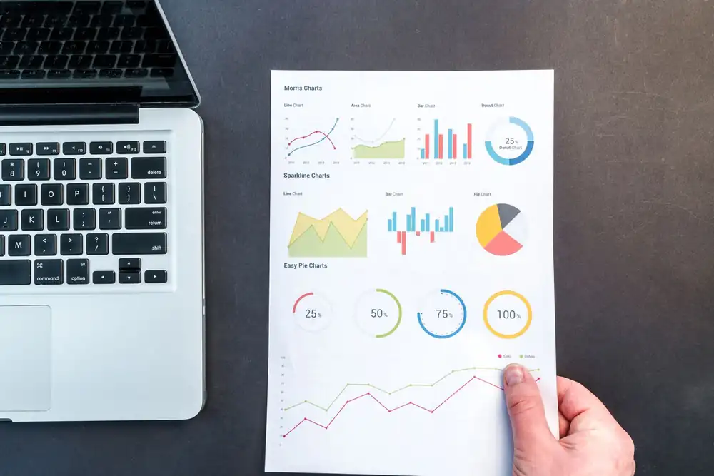 Printed statistical charts and graphs being reviewed beside a laptop
